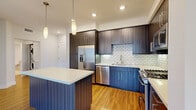 Located at 13385 Highlands Pl in San Diego's desirable Carmel Valley neighborhood (92130), this single-story residence offers a well-designed layout with modern finishes throughout. The kitchen is a standout feature, showcasing rich dark wood cabinetry, bold navy lower cabinets, a white subway tile backsplash, quartz countertops, and a central island with pendant lighting overhead. Stainless steel appliances — including a French door refrigerator, dishwasher, and gas range — complete the space. In-unit stacked laundry is also conveniently located nearby. The open living and dining area flows seamlessly from the kitchen, featuring warm hardwood-style flooring and a ceiling fan. Bedrooms are bright and airy, with large windows offering views of surrounding palm trees and neighboring architecture; one room features hardwood-style flooring with outdoor access, while another offers plush carpeting and a spacious walk-in closet with built-in shelving. The bathrooms are finished in a clean, contemporary style — one includes a soaking tub with tiled surround and a dark wood vanity, while another features a floor-to-ceiling marble-tiled walk-in shower with frameless glass enclosure. Recessed lighting and neutral tones create a bright, cohesive ambiance throughout the entire space.