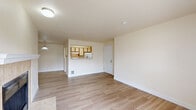 Located in Bothell, WA, this two-bedroom, two-bathroom residence offers a thoughtfully laid-out single-level floor plan. The open-concept living, dining, and kitchen area serves as the heart of the home, featuring light hardwood-style flooring that runs throughout the main living spaces. The living room is highlighted by a tile-surround fireplace and sliding glass doors that open to an outdoor balcony, filling the space with natural light. A pass-through window connects the living and dining area to the galley-style kitchen, which is equipped with ample cabinetry, a full suite of white appliances, a stainless steel sink, and light countertops. A dedicated hallway leads to the two bedrooms, each carpeted and featuring large windows that bring in natural light and offer neighborhood views. Baseboard heaters are present in the bedrooms for comfortable climate control. The two bathrooms include vanities with generous countertop space and large mirrors, complemented by hardwood-style flooring. Four closets provide substantial storage throughout the unit, and a dedicated laundry area adds everyday convenience. The neutral, warm color palette and clean finishes give the entire residence a bright and welcoming ambiance.