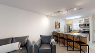 Located at 2309 Evermore Way in Wilmington, NC, this single-floor unit offers a well-designed, functional layout with a clean, contemporary aesthetic throughout. The open-concept living and dining area flows seamlessly into the kitchen, creating a comfortable and connected common space. The living area features plush carpeting and dark leather seating, complemented by track lighting overhead that illuminates the room effectively. A wall-mounted shelf adds a touch of character near the transition to the kitchen.

The kitchen is equipped with stainless steel appliances, including a refrigerator, microwave, and range, set against warm wood cabinetry. A peninsula with bar-height seating and a built-in sink serves as both a food prep area and a casual dining space, making it ideal for everyday use.

The unit includes two bedrooms, each finished with neutral tones, soft carpeting, and windows that bring in natural light with views of surrounding greenery. Both rooms offer ample space for bedroom furniture and personal storage.

The bathroom features tile flooring, a wood-toned vanity, and a tub-shower combination enclosed by sliding glass doors, providing a clean and practical design. Overall, this unit presents a straightforward, move-in-ready living space in a convenient Wilmington location.