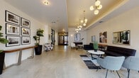 Located in Philadelphia's 19123 zip code, this contemporary lobby offers a well-appointed first impression with a thoughtfully designed interior that balances industrial and modern aesthetics. Polished concrete floors span the entire space, lending a sleek, urban character that complements the crisp white walls throughout.

The lobby is anchored by multiple distinct seating areas, each carefully arranged to encourage both social interaction and individual comfort. Clusters of black sofas, patterned accent chairs, and marble-topped coffee tables are positioned atop layered geometric rugs, creating defined zones within the open floor plan. A series of globe pendant chandeliers with brass fittings cascade from a coffered ceiling detail, providing warm, ambient illumination that contrasts elegantly with the industrial flooring below.

Large black-framed glass doors and windows facing the street flood the interior with natural light and provide views of the surrounding Philadelphia streetscape. Curated artwork—including abstract paintings and a gallery-style grid of framed photography—adorns the walls, adding cultural depth to the space. Lush fiddle-leaf fig plants and ornamental grasses introduce natural elements throughout. Black-framed interior glass doors provide visual connectivity deeper into the building, reinforcing the lobby's open and inviting atmosphere.