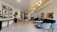 Located in Philadelphia's 19123 zip code, this contemporary lobby offers a well-appointed first impression with a thoughtfully designed interior that balances industrial and modern aesthetics. Polished concrete floors span the entire space, lending a sleek, urban character that complements the crisp white walls throughout.

The lobby is anchored by multiple distinct seating areas, each carefully arranged to encourage both social interaction and individual comfort. Clusters of black sofas, patterned accent chairs, and marble-topped coffee tables are positioned atop layered geometric rugs, creating defined zones within the open floor plan. A series of globe pendant chandeliers with brass fittings cascade from a coffered ceiling detail, providing warm, ambient illumination that contrasts elegantly with the industrial flooring below.

Large black-framed glass doors and windows facing the street flood the interior with natural light and provide views of the surrounding Philadelphia streetscape. Curated artwork—including abstract paintings and a gallery-style grid of framed photography—adorns the walls, adding cultural depth to the space. Lush fiddle-leaf fig plants and ornamental grasses introduce natural elements throughout. Black-framed interior glass doors provide visual connectivity deeper into the building, reinforcing the lobby's open and inviting atmosphere.