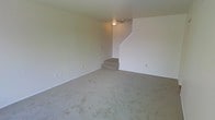 This multi-level residence is spread across three floors, offering a versatile and spacious layout suited for a variety of living arrangements. The main living area is finished with wall-to-wall carpeting in a neutral tone, creating a warm and understated ambiance throughout. Smooth, light-painted walls contribute to a clean, bright aesthetic, while a ceiling-mounted light fixture provides practical overhead illumination. A carpeted staircase rises from the main living space, connecting the floors with a straightforward and efficient design. The open layout of the living area allows for flexible furniture arrangements and a sense of openness. The consistent use of neutral tones — from the walls to the flooring — gives the space a cohesive and move-in-ready feel. With three full floors, the home provides ample room for distinct living, sleeping, and utility zones, making it a functional and adaptable residence. The understated design choices throughout allow new occupants to personalize the space to their own taste.