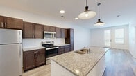 Located at 234 E Main St in Plainfield, Indiana, this two-bedroom, one-bathroom residence offers a thoughtfully designed single-level layout with contemporary finishes throughout. The open-concept kitchen and living area serves as the heart of the home, anchored by a large granite-topped island with an undermount sink and stylish pendant lighting overhead. Rich dark-brown shaker cabinetry lines the kitchen walls, complemented by a white subway tile backsplash and a full suite of stainless steel appliances, including a refrigerator, electric range, and built-in microwave. Light wood-look plank flooring flows throughout the main living areas, creating a bright and cohesive feel. The living room benefits from natural light through a glass-panel door. The full bathroom features a tiled tub-shower combo, granite vanity countertop, and dark cabinetry consistent with the kitchen's design. Both bedrooms are carpeted and offer natural light via windows with blinds. A dedicated laundry area houses a stacked washer and dryer unit alongside a water heater. The space also includes a closet for additional storage. Clean white walls and modern black hardware accents lend a fresh, move-in-ready aesthetic throughout.