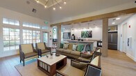 This single-floor community clubhouse is thoughtfully designed to offer a range of amenities within a cohesive, modern aesthetic. The central lounge area serves as the heart of the space, anchored by a statement sputnik chandelier suspended from a raised tray ceiling. Comfortable seating arrangements — including a tufted sofa accented with botanical print pillows and a set of upholstered armchairs — are centered around a marble-top coffee table atop a woven area rug, all set over warm hardwood flooring.

Framed by a natural wood beam, the café bar area flows seamlessly from the lounge, featuring white shaker cabinetry with gold hardware, a herringbone-patterned tile backsplash, and a commercial-grade coffee station. Vibrant botanical artwork adds a pop of color to this functional yet stylish space.

Adjacent to the main lounge, a dedicated media nook showcases a wall-mounted flat-screen television set against bold geometric-patterned wallcovering, paired with mid-century modern lounge chairs.

A standout conference area is bathed in natural light through floor-to-ceiling arched and gridded windows, offering views of the surrounding landscape. A sleek wood conference table with leather-upholstered chairs creates an ideal setting for meetings or focused work.

Accessible directly from the lounge, a well-equipped fitness center with cardio machines completes this versatile and inviting community space.