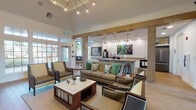 This single-floor community clubhouse is thoughtfully designed to offer a range of amenities within a cohesive, modern aesthetic. The central lounge area serves as the heart of the space, anchored by a statement sputnik chandelier suspended from a raised tray ceiling. Comfortable seating arrangements — including a tufted sofa accented with botanical print pillows and a set of upholstered armchairs — are centered around a marble-top coffee table atop a woven area rug, all set over warm hardwood flooring.

Framed by a natural wood beam, the café bar area flows seamlessly from the lounge, featuring white shaker cabinetry with gold hardware, a herringbone-patterned tile backsplash, and a commercial-grade coffee station. Vibrant botanical artwork adds a pop of color to this functional yet stylish space.

Adjacent to the main lounge, a dedicated media nook showcases a wall-mounted flat-screen television set against bold geometric-patterned wallcovering, paired with mid-century modern lounge chairs.

A standout conference area is bathed in natural light through floor-to-ceiling arched and gridded windows, offering views of the surrounding landscape. A sleek wood conference table with leather-upholstered chairs creates an ideal setting for meetings or focused work.

Accessible directly from the lounge, a well-equipped fitness center with cardio machines completes this versatile and inviting community space.