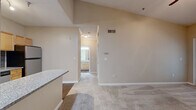 This efficiently designed 1-bedroom, 1-bathroom single-floor unit offers a thoughtful layout across a compact but functional footprint. The living area impresses with soaring vaulted ceilings, a ceiling fan, and elegant French doors that open to an outdoor space while flooding the room with natural light. Neutral-toned carpet and warm beige walls create a cohesive, inviting ambiance throughout.

The kitchen is a standout feature, equipped with light maple cabinetry, granite countertops, a gray subway tile backsplash, stainless steel appliances including a refrigerator and dishwasher, and a peninsula that provides additional prep and seating space. Durable wood-look flooring anchors the kitchen and connects to the hallway.

The bedroom is generously proportioned, featuring its own ceiling fan, plush carpeting, and a large window with verdant outdoor views. A dedicated closet provides practical storage. The bathroom includes a tiled shower/tub combo, wood-look flooring, granite vanity countertop, and warm wood cabinetry.

A dedicated laundry room with washer/dryer hookups and shelving adds everyday convenience, while a hallway connects all areas seamlessly. The unit combines functional design with modern finishes throughout.
