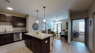 This single-story residence is designed with a cohesive, modern aesthetic, highlighted by light wood-style flooring, neutral gray walls, and dark espresso cabinetry throughout. The kitchen serves as a central hub of the layout, outfitted with rich dark cabinetry extending to the ceiling, granite countertops, a full suite of stainless steel appliances, and a large granite-topped island with bar seating beneath stylish pendant lighting. The open layout allows the kitchen to flow seamlessly into the living area, which features a ceiling fan, natural light from large French doors, and outdoor views through slatted blinds.

The unit includes two bedrooms, each carpeted or with wood-style flooring, and fitted with windows that bring in natural light and views of surrounding greenery. The primary bathroom offers a granite-topped double vanity with dark cabinetry, a tiled walk-in shower, and a separate walk-in closet. The secondary bathroom features a tiled tub-shower combination and granite countertop. A dedicated utility room includes washer/dryer hookups, a water heater, and wire shelving for additional storage.