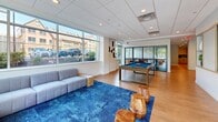 Located at 5901 Montrose Rd in Rockville, MD, this generously sized single-floor amenity space offers a thoughtfully designed layout with distinct zones tailored for socializing, recreation, focused work, and family use. The open-concept interior features warm wood-look flooring throughout, recessed lighting, and a cohesive modern aesthetic accented by bold blue tones and lush greenery.

The main lounge and game room area is anchored by a full-size pool table and a plush sectional sofa set atop a vibrant blue area rug, with large windows that flood the space with natural light and provide outdoor views. Adjacent to this is a spacious dining and gathering area featuring a long conference-style table with blue velvet chairs, complemented by smaller café-style seating along a textured blue accent wall adorned with curated artwork.

A fully equipped kitchen offers wood-toned cabinetry, white quartz countertops, a blue tile backsplash, and stainless steel appliances including a refrigerator and microwave. A compact private workstation with a built-in wood desk, natural light, and blue-toned carpet tile provides a quiet retreat. The children's room is bright and playful, featuring colorful striped walls, low shelving with books and activities, and child-sized furniture. Glass-panel partitions with black framing elegantly define zones while maintaining an open, airy feel throughout.
