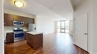 Located at Harbor Point in Stamford, CT, this one-bedroom, one-bathroom residence offers a thoughtfully designed open-concept layout with rich hardwood flooring throughout the main living areas. The combined kitchen and living room serves as the heart of the home, featuring a sleek, modern kitchen outfitted with dark wood cabinetry, crisp white countertops, a central island, and a full suite of stainless steel appliances including a gas range, dishwasher, microwave, and refrigerator. Floor-to-ceiling windows and a glass door flood the living area with natural light and frame sweeping views of Stamford Harbor and the surrounding waterfront landscape. The spacious bedroom continues the view experience with its own floor-to-ceiling window overlooking the harbor, and is finished with plush carpeting. A generous walk-in closet with wire shelving provides ample storage, complemented by an additional closet. The bathroom features a full tub-shower combination with clean white tile, set against neutral-toned flooring and warm cabinetry. An in-unit laundry area adds everyday convenience. The overall ambiance is clean, contemporary, and bright, with a strong connection to the waterfront setting.