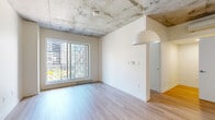 Located at 300 Avenue de l'Équinoxe in Brossard, Quebec, this well-appointed 2-bedroom, 1-bathroom unit offers a contemporary urban living experience. The space is defined by a striking combination of exposed concrete ceilings and light hardwood flooring that runs throughout, creating an industrial-modern aesthetic balanced by crisp white walls and an abundance of natural light.

The kitchen is a standout feature, boasting sleek white cabinetry that extends to the ceiling, a classic tile backsplash, stainless steel appliances including a refrigerator and range, and a generous island with an integrated sink — ideal for both cooking and casual dining.

The open living area is bright and airy, with large windows framing views of the surrounding urban landscape and allowing ample daylight to fill the space. Both bedrooms are well-sized, each featuring large windows with city views, light hardwood floors, exposed concrete ceilings, and clean-lined flush doors that maintain a cohesive modern feel.

The bathroom is finished to a high standard, featuring large-format tile flooring, a soaking tub with a glass sliding enclosure, a wall-mounted toilet, a floating vanity, and a backlit mirror that adds a refined, contemporary touch. A hallway connects all rooms efficiently, completing this thoughtfully designed urban residence.