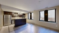 Located at 1212 Griswold St in the heart of Detroit, MI, this efficiently designed unit offers a thoughtfully organized single-floor layout. The open-plan living, dining, and kitchen area forms the centerpiece of the space, maximizing functionality without sacrificing style. The kitchen is outfitted with rich dark espresso cabinetry, stainless steel appliances including a refrigerator, dishwasher, microwave, and range, as well as a large central island with a light stone countertop and pendant lighting overhead. Light-toned large-format tile flooring runs throughout, lending a clean and cohesive aesthetic. The living and dining area benefits from multiple windows that invite natural light and offer views of the surrounding urban streetscape. Warm neutral wall tones create an inviting ambiance throughout. The full bathroom features a dark vanity with a stone countertop, built-in shelving, tile flooring with a mosaic border detail, and a glass-enclosed stand-up shower. Two closets provide practical storage solutions, while a hallway connects the space seamlessly. The overall design balances modern urban living with practical, well-appointed interiors suited for downtown Detroit life.