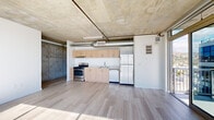 Located at 1522 Gordon Street, this modern urban residence offers three bedrooms and one bathroom across a single thoughtfully designed floor. The space embraces an industrial-contemporary aesthetic, defined by exposed concrete ceilings, visible ductwork, and light wood-tone flooring that runs throughout. The open-concept kitchen is equipped with stainless steel appliances — including a gas range, dishwasher, and refrigerator — complemented by light wood cabinetry and a clean white backsplash, all beneath striking exposed concrete overhead. Floor-to-ceiling windows in the living and bedroom areas flood the space with natural light and frame sweeping panoramic city views, creating a bright and airy atmosphere. The primary bedroom is generously proportioned, featuring expansive glazing and a sliding closet. The additional bedrooms offer their own character — one showcasing raw concrete accent walls that reinforce the industrial design language, and another with large windows overlooking the urban skyline. A hallway leads to an in-unit stacked washer and dryer, adding everyday convenience. The full bathroom is cleanly finished with large-format tile flooring, a warm wood vanity, and a combination tub and shower. This unit delivers a compelling blend of urban edge and modern comfort.