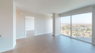 Located on the 14th floor at 8800 Lombard in San Diego, this contemporary residence is defined by its clean, modern aesthetic and sweeping views of the surrounding cityscape and beyond. Light wood-tone flooring flows throughout the open living areas, complementing a neutral color palette of crisp whites and warm taupes that lend the space an airy, understated elegance.

Floor-to-ceiling glass windows dominate multiple rooms, flooding the interior with abundant natural light and framing expansive panoramic views of San Diego's treetops, neighborhoods, and distant terrain. The living area is generously proportioned, with a structural column adding architectural character without interrupting the open feel.

The kitchen features a galley-style layout with tall, textured light wood cabinetry extending to the ceiling, stainless steel appliances including a gas range and built-in refrigerator, and a central island with clean countertops. Recessed lighting provides consistent illumination throughout.

Two bathrooms serve the residence. The primary bath includes a frameless glass walk-in shower with tile surround, vertical LED lighting panels, and an adjacent walk-in closet. The secondary bath offers a soaking tub with tile surround, an extended vanity with an undermount sink, and access to an additional walk-in closet. Additional rooms feature hardwood flooring, clean white walls, and continued access to the building's impressive elevated views.