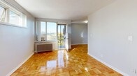 This 3-bedroom, 1-bathroom residence offers a practical and comfortable layout across a single floor, connected by two hallways that guide you through the space. The living room serves as the heart of the home, featuring gleaming parquet hardwood flooring and direct access to a balcony through a full-length glass door, inviting an abundance of natural light and outdoor views of surrounding greenery. A radiator provides reliable in-unit heating throughout.

Each of the three bedrooms continues the warm parquet flooring theme and is painted in soft, neutral tones. The primary bedroom offers a dedicated closet with classic double doors, while the secondary bedrooms feature windows that frame pleasant tree-lined views. The rooms are well-proportioned, with the primary bedroom providing a cozy yet functional footprint.

The bathroom is a standout feature, finished with elegant marble-style wall tiles surrounding the bathtub and shower combination, complemented by chrome fixtures and a wall-mounted mirror cabinet — a clean, refined aesthetic throughout.

Two hallways connect the rooms efficiently, contributing to a logical flow between living and private spaces. Consistent parquet flooring and a light, neutral color palette lend the entire residence a cohesive and inviting character.