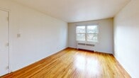 Located at 251 Hillcrest Manor Ct in Utica, NY, this two-bedroom, one-bathroom unit offers a practical and well-organized single-floor layout. Warm, polished hardwood floors run throughout the living areas and bedrooms, lending a consistent and inviting character to the space. Each bedroom is naturally lit by double-hung windows that frame outdoor neighborhood views, with classic baseboard radiators providing in-unit heating. The primary bedroom is generously sized and includes a closet and direct access to the bathroom, adding a layer of convenience. The living area features a bright, open feel with a second entry door and an additional window that draws in natural light. The kitchen is compact and efficiently arranged, featuring white cabinetry, wood-toned countertops, a stainless steel sink, and a gas range, providing essential functionality. The bathroom includes a full tub-shower combination with classic pink tile wainscoting and black accent trim, reflecting a retro aesthetic. A connecting hallway ties the rooms together in a cohesive flow. Overall, this unit offers a straightforward and livable layout with consistent finishes throughout.