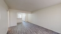This single-floor, 3-bedroom, 1-bathroom unit offers a practical and efficient layout designed to maximize every square foot. The combined kitchen and living room serves as the heart of the home, featuring durable laminate wood-style flooring in a cool gray tone, a textured ceiling, and a large window that invites natural light into the living area. The kitchen is equipped with white cabinetry, a peninsula counter with a built-in sink, and white appliances, including a refrigerator. A windowed exterior door provides direct access and adds brightness to the space.

The three bedrooms are carpeted for comfort and each features a ceiling fan with a light fixture. The primary bedroom includes a closet and a window with vertical blinds. A dedicated closet room offers built-in shelving units, providing organized storage space. The shared full bathroom is clean and functional, featuring white subway-tiled walls surrounding a full bathtub and shower combination, a toilet, a vanity with a countertop sink, and wood-style flooring. A central hallway connects the bedrooms and bathroom, ensuring a logical and efficient flow throughout the unit.