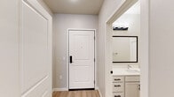 This efficient single-floor unit offers a thoughtfully arranged layout comprising a hallway, kitchen, bedroom, and bathroom. Light wood-style vinyl flooring runs consistently throughout, complementing the soft neutral tones of the walls and crisp white trim to create a clean, cohesive aesthetic.

The kitchen is a standout feature, showcasing white shaker-style cabinetry with matte black hardware, a herringbone-patterned white tile backsplash, and light quartz countertops. A full suite of stainless steel appliances — including a range, microwave, dishwasher, and refrigerator — provides a modern, functional workspace, while under-cabinet lighting adds both practicality and ambiance.

The entry hallway is welcoming, anchored by a solid white paneled door with a keypad lock. A glimpse into the bathroom from the entry reveals a well-appointed vanity with white cabinetry and black hardware. The full bathroom features a tub-shower combination, a white vanity with storage, and continued light flooring, maintaining the unit's consistent design language.

The bedroom is a quiet, neutral space with smooth walls and ample room for furnishings. A separate utility area with an electrical panel is accessible off the hallway. Overall, the unit presents a modern, move-in-ready space with consistent, quality finishes throughout.
