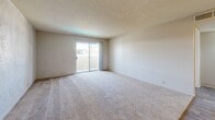 Located at 3111 E Fourth St in Tucson, AZ, this one-bedroom, two-bathroom unit offers a practical and comfortable single-floor layout. The living room is generously proportioned, featuring neutral carpet flooring, textured walls, a popcorn ceiling, and a sliding glass door that opens to a balcony, allowing natural light to fill the space. Adjacent to the living area, the entry zone features wood-look hard flooring that transitions into the kitchen. The kitchen is efficiently laid out with warm wood-toned cabinetry, white appliances including a refrigerator, electric range, and dishwasher, along with light-colored countertops and wood-look vinyl flooring. The spacious primary bedroom is carpeted and provides ample room for furnishings, with a dedicated closet for storage. The two bathrooms are well-appointed: one features a full tub-shower combo with white tile surround and wood-look flooring, while the other includes a wide vanity with warm wood cabinetry, a large mirror with overhead lighting, and matching flooring. A hallway connects the rooms, contributing to the unit's efficient flow. Textured walls and neutral tones throughout lend the space a cohesive, understated character.