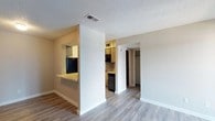 This single-floor residence offers a practical and well-organized layout designed for comfortable everyday living. The main living area features smooth, wood-look laminate flooring that extends throughout the space, providing a cohesive and clean aesthetic. A textured popcorn ceiling adds a classic touch overhead, while neutral wall tones keep the interior bright and versatile.

The kitchen is partially open to the living area via a pass-through counter finished with a granite-style surface, allowing for easy interaction between the two spaces. The kitchen itself is equipped with dark appliances, including a refrigerator and microwave, and features cabinetry that offers ample storage. A dedicated hallway leads from the living area into the deeper parts of the residence, providing access to a closeted bedroom and an additional room beyond.

The open corridor layout creates a natural flow between the living, kitchen, and private areas of the home. The built-in closet visible from the hallway adds functional storage without sacrificing space. Overall, the residence presents a straightforward, no-frills design that prioritizes functionality and ease of movement, making it a well-suited space for a range of occupants.