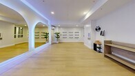 Located at 2132 Wilkinson Street in Kelowna, BC, this thoughtfully designed studio space offers a clean, contemporary environment well-suited for yoga, fitness, or wellness practices. The single open-plan floor is finished with warm, light hardwood flooring that extends throughout, creating a bright and welcoming atmosphere.

The studio's most striking architectural feature is a series of elegantly arched mirrors along one wall, each framed with soft LED backlighting that casts a gentle blue-purple ambient glow across the white walls and ceiling. This lighting design lends the space a calm, modern aesthetic that enhances its function as a wellness environment.

Recessed ceiling lighting supplements the ambient illumination, ensuring the space is evenly and cleanly lit. Wall-mounted storage racks — ideal for yoga mats or rolled towels — are neatly arranged along one wall, providing practical organization for studio equipment. A wall-mounted split air conditioning unit ensures comfortable climate control year-round.

Additional details include wooden benches for seating near the entrance, a dedicated equipment shelf stocked with yoga blocks and accessories, and tasteful greenery in the form of potted tropical plants that add a touch of nature to the interior. The overall ambiance is serene, minimal, and purposeful — a refined space designed to support focus and well-being.