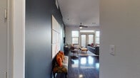 This thoughtfully designed single-floor residence combines modern aesthetics with functional living across a well-organized layout. The open-concept living area greets you with rich, dark hardwood floors that extend throughout the main living spaces, complemented by a ceiling fan and multiple windows with transom panes that flood the room with natural light. A French door leads to an exterior balcony, enhancing the sense of openness. The living room is anchored by a comfortable seating arrangement and a natural wood coffee table set atop a patterned area rug.

The gourmet kitchen is a standout feature, showcasing rich dark cabinetry, granite countertops, stainless steel appliances, under-cabinet lighting, and a large center island with bar seating. Pendant and track lighting complete the refined culinary space.

The primary bedroom is defined by a striking dark accent wall, a bold red upholstered headboard, ceiling fan, plush carpeting, and a window offering outdoor views. The en-suite bathroom features granite countertops, dark wood cabinetry, and tile flooring. A second bedroom offers its own ceiling fan, natural light, and soft carpeting. A second full bathroom includes a tiled tub-shower combination and matching granite vanity finishes.