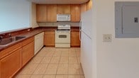 Located on the third floor at 601 Riverside Ave in Lyndhurst, NJ, this apartment offers a practical and comfortable single-floor layout. The living area features neutral-toned carpeting and warm beige walls, creating a bright and inviting atmosphere. A pass-through counter connects the living and dining area to the kitchen, promoting an open feel while maintaining defined spaces. The kitchen is equipped with warm wood cabinetry, dark countertops, tile flooring, and white appliances including a refrigerator, electric range, built-in microwave, and dishwasher — providing full functionality in a compact footprint. The bedroom is generously proportioned with plush carpeting, a large multi-pane window that fills the room with natural light and outdoor views, and a wall-mounted HVAC unit for climate control. An additional carpeted room offers flexibility as a second bedroom or dedicated living space, also featuring natural light through a window. The full bathroom includes tile flooring, a wood-vanity with a mirror cabinet, and a tub-shower combination with tile surround. Throughout the unit, clean white trim and consistent warm tones contribute to a cohesive and move-in-ready aesthetic.