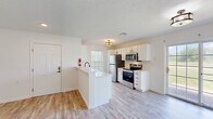 This well-designed single-story home offers a thoughtful layout across two bedrooms and two bathrooms, presenting a clean, move-in-ready aesthetic with modern finishes throughout. The open-concept kitchen and living area forms the heart of the home, where a peninsula with a white countertop provides both prep space and a casual seating area. The kitchen is outfitted with white shaker-style cabinetry, stainless steel appliances including a refrigerator, over-the-range microwave, and electric range, all complemented by light wood-look luxury vinyl plank flooring that extends through the main living areas. Large windows in the living room invite generous natural light and offer views of the outdoors, enhancing the airy, open feel of the space. A hallway leads to the private quarters, where both bedrooms feature ceiling fans, soft carpeting, and individual closets. The spacious primary bedroom is notably comfortable in size and includes a window for natural light. The two bathrooms are finished with white cabinetry, solid-surface countertops, and matte black hardware — one featuring a full tub/shower combo, and the other a compact vanity with a mirror and rustic wood light fixture. Textured ceilings and consistent neutral tones throughout give the home a cohesive, welcoming character.