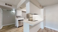 This single-floor residence offers a clean, modern aesthetic throughout, with thoughtful finishes and a practical layout. The kitchen is a standout feature, designed in a galley style with crisp white cabinetry, granite-look countertops, a gray subway tile backsplash, and a full suite of stainless steel appliances including a refrigerator, dishwasher, and electric range. A peninsula with a built-in cooktop and overhead range hood extends the workspace and provides a natural divider between the kitchen and the main living area. Light wood-look flooring flows through the kitchen and living spaces, lending a bright, cohesive feel. The living area is open and airy, benefiting from a large sliding glass door that leads to a private balcony, filling the room with natural light and offering views of the surrounding outdoors. The bedrooms are carpeted for comfort and warmth, each featuring windows with blinds that allow for natural light while maintaining privacy. Neutral gray walls and white trim are consistent throughout the unit, creating a calm and versatile backdrop. Textured ceilings are present throughout the space, adding a classic residential character to the overall interior.