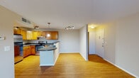 Located at 5714 Ravens Crest Dr in Plainsboro, NJ, this single-floor residence offers a thoughtfully designed layout with a seamless blend of comfort and practicality. The open-concept living and kitchen area serves as the heart of the home, unified by warm hardwood-style flooring that extends throughout the main spaces. The kitchen is well-equipped with rich honey-toned wood cabinetry, dark granite-style countertops, stainless steel appliances including a range and refrigerator, and a curved peninsula that doubles as a breakfast bar. Track lighting and a pendant light overhead add both task illumination and visual warmth. The living area is generously proportioned, bathed in natural light, and flows effortlessly from the kitchen toward the main entry. Bedrooms feature plush carpeting and windows with blinds that allow for natural light and views of the surrounding greenery. The bathroom is clean and functional, appointed with a warm wood vanity, white countertop, a large mirror with vanity lighting, and a full tub-shower combination. The overall ambiance is bright, neutral, and move-in ready, making this Plainsboro residence a practical and inviting place to call home.