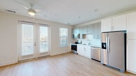 Located at 4939 Ohear Ave in North Charleston, SC, this efficiently designed single-floor unit offers a thoughtful layout that maximizes its cozy footprint. The open-concept kitchen and living area serves as the heart of the space, filled with natural light streaming through multiple windows and French doors that lead to an outdoor balcony. A ceiling fan overhead keeps the space comfortable year-round.

The kitchen is well-appointed with two-tone cabinetry — white lower cabinets paired with gray upper cabinets — set against a clean white subway tile backsplash. A full suite of stainless steel appliances includes a refrigerator with ice and water dispenser, electric range, over-the-range microwave, and dishwasher, providing everything needed for everyday cooking.

Light wood-tone flooring runs consistently throughout the unit, lending warmth and visual continuity from the entry hallway through the living area. The hallway provides access to additional storage closets, keeping the living spaces uncluttered.

The bathroom features a clean, modern aesthetic with a white vanity, undermount sink, framed mirror, and a full tub-shower combo with white tile surround and brushed nickel fixtures. Matching wood-tone flooring ties the bathroom seamlessly to the rest of the unit. Overall, the space presents a bright, clean, and move-in-ready environment.