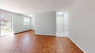 This thoughtfully laid-out one-bedroom, one-bathroom unit spans a compact yet efficient single floor, making excellent use of every square foot. Throughout the main living areas and bedroom, rich warm-toned parquet hardwood flooring adds a distinctive character that ties the space together cohesively.

The open living room is a bright and airy space, benefiting from a large sliding glass patio door that floods the room with natural light and provides direct views of the surrounding greenery. An additional window further enhances the sense of openness. Baseboard heating is present throughout, ensuring comfortable temperatures year-round.

The galley-style kitchen is efficiently designed with ample white cabinetry lining both walls, offering generous storage and counter space. It is equipped with a standard electric range and a refrigerator, complemented by a stainless steel sink. The clean, all-white palette gives the kitchen a bright, functional feel.

The bedroom is a well-proportioned private retreat, featuring a large built-in closet with bi-fold doors, a window with outdoor views, and the same warm parquet flooring found throughout the unit. A connecting hallway leads to the full bathroom, which includes a tiled tub-shower combination with chrome fixtures. The entry hallway provides a practical transition from the front door into the main living space.