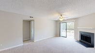 Located at 1108 Saint Andrews Dr in Wilmington, NC, this single-floor home offers five bedrooms and two full bathrooms. The combined kitchen and living room area serves as the heart of the home, with the living room featuring plush carpeting, a ceiling fan, a wood-burning fireplace with a clean white mantle, and sliding glass door access to a private balcony with outdoor views. A second room also opens to a balcony, providing additional outdoor access and natural light. The kitchen is well-appointed with white shaker-style cabinetry, dark countertops, light wood-look flooring, stainless steel appliances including a range and refrigerator, and a built-in sink with a peninsula. The five bedrooms are carpeted and finished in neutral tones, with windows allowing natural light throughout. At least one bedroom features a walk-in closet. The two bathrooms include wood-look tile flooring, white vanity cabinetry, and a tub-shower combination. Textured ceilings are present throughout the home. Two hallways and two closets round out the functional layout, providing ample circulation and storage space across the well-organized floor plan.