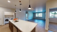 This single-floor unit is designed with a contemporary open-concept layout that seamlessly connects the kitchen, dining, and living areas. The kitchen serves as a central highlight, featuring a large island with a white quartz countertop, an undermount sink, and stylish pendant lighting overhead. Two-toned cabinetry pairs dark wood lower cabinets with crisp white upper cabinets, complemented by a subway tile backsplash and a full suite of stainless steel appliances, including a gas range, built-in microwave, and French door refrigerator. Light wood-style flooring runs throughout the main living areas, adding warmth to the open space, which benefits from natural light through a wide window and an exterior door leading outside. An in-unit washer and dryer are conveniently accessible from both the kitchen corridor and the main living area. Two carpeted bedrooms each feature ceiling fans and windows with outdoor views. The two bathrooms are finished with white vanity cabinetry, quartz countertops, and light wood-style flooring; one includes a glass-enclosed walk-in shower, while the other features a tub-shower combination with a large vanity mirror.