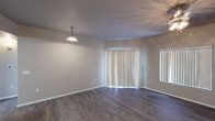 Located in Queen Creek, Arizona, this single-story home offers a well-designed layout with a consistent, modern aesthetic throughout. The main living area is open and airy, featuring rich dark hardwood-style flooring that extends through the common spaces. A pendant light fixture adds a subtle decorative touch, while sliding glass doors and large windows dressed with vertical blinds invite abundant natural light and provide outdoor views.

The entryway opens conveniently to both the living space and the kitchen, which is configured in a classic galley style. The kitchen is equipped with white cabinetry, dark granite-style countertops, a double basin sink, electric range, built-in microwave, and dishwasher. A pass-through window connects the kitchen to the adjacent living area, enhancing the sense of openness. In-unit laundry hookups are accessible from the kitchen corridor.

The bedroom features plush carpeting, a large window with vertical blinds allowing ample natural light, and neutral wall tones that create a calm, restful environment. The bathroom is appointed with wood-look tile flooring, a granite-topped vanity with white cabinetry, and a full tub and shower combination with clean white tile surround. Throughout the home, neutral gray walls and white trim provide a clean, cohesive backdrop suited to a variety of interior styles.