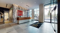 This vibrant amenity floor makes a bold first impression through its lobby, where a dramatic graffiti-style mural wall serves as a backdrop to a sleek wood-and-metal reception desk. Large floor-to-ceiling windows flood the entry with natural light and offer views of the surrounding streetscape, while large-format tile flooring anchors the space with a clean, modern aesthetic.

Beyond the lobby, the common areas unfold into a series of thoughtfully designed lounges. One gathering space features an exposed dark ceiling, a linear fireplace, a wall-mounted television, and an eclectic mix of seating — from tufted sofas to patterned armchairs — creating a relaxed yet sophisticated atmosphere. A second lounge offers warm wood-paneled walls with built-in bench seating, colorful accent pillows, and curated artwork, providing an intimate and inviting retreat.

A central corridor connects additional amenity spaces, including glass-enclosed conference and meeting rooms furnished for productive collaboration. Private nook seating and decorative area rugs add texture and personality throughout.

The fitness center is generously proportioned, offering an extensive array of Matrix strength machines and cardio equipment, including treadmills and ellipticals, all beneath a dark coffered ceiling with ample natural light from floor-to-ceiling windows along one side.