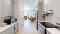 Located at 2613 Montgomery St in the heart of Savannah, Georgia, this thoughtfully designed one-bedroom, one-bathroom residence offers a complete and functional living experience within a compact single-floor layout.

The galley-style kitchen is sleekly appointed with sage-green cabinetry, white quartz countertops, light hardwood-style flooring, and stainless steel appliances including a refrigerator, electric range, dishwasher, and microwave. Open shelving adds both practicality and a modern aesthetic, while recessed lighting keeps the space bright and welcoming. The kitchen flows naturally toward a combined living and dining area, visible through the corridor, where a ceiling fan and generous windows allow ample natural light to fill the space.

The spacious primary bedroom is a serene retreat, featuring large windows and a glass-paned door that open to outdoor views of lush greenery, inviting abundant natural light. Light hardwood flooring, neutral walls, and a comfortable sitting area with a loveseat contribute to the room's calm, airy ambiance.

The bathroom is designed with accessibility in mind, equipped with grab bars throughout, a vanity with under-cabinet storage, tile flooring, and a shower with a curtain enclosure. The clean, neutral palette maintains a consistent sense of comfort and ease throughout the entire residence.