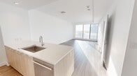 Located in Calgary, AB, this modern 1-bedroom, 1-bathroom unit offers a thoughtfully designed open-concept layout finished with light wood-grain flooring throughout. The combined kitchen and living area is bright and airy, anchored by a sleek kitchen island with a white quartz countertop and undermount sink. The kitchen is well-appointed with light wood cabinetry, stainless steel appliances including a full-size refrigerator, built-in oven, microwave, and gas cooktop. Floor-to-ceiling windows in the living area and bedroom flood the space with natural light while framing panoramic views of the Calgary cityscape. The spacious primary bedroom features large sliding glass doors that open to the outdoors, a closet, and generous proportions. An in-suite washer and dryer add everyday convenience. The bathroom is elegantly finished with marble-style porcelain tile on both the floors and walls, a soaker tub with shower, a floating vanity with an undermount sink, and a large mirror. Clean white walls, recessed lighting, and a minimalist modern aesthetic tie the entire unit together into a cohesive, contemporary living space.