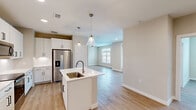Located at 4103 Rogers Rd in San Antonio, TX, this well-designed single-story home offers 2 bedrooms and 2 bathrooms within a thoughtfully laid-out floor plan. The open-concept kitchen and living area serves as the heart of the home, featuring white shaker-style cabinetry, quartz countertops, a center island with a single-basin sink, stainless steel appliances — including a French door refrigerator, electric range, and built-in microwave — and elegant pendant lighting. Light wood-look flooring flows seamlessly throughout the entire space, enhancing the bright, cohesive feel. The living and dining areas benefit from natural light through large windows and a glass-paneled door leading to an outdoor area. Both bedrooms are generously sized, each equipped with ceiling fans and large windows that invite natural light and outdoor views. The primary bedroom includes access to a spacious walk-in closet with wrap-around shelving and rod systems providing ample storage. The second bedroom also features its own closet. Both bathrooms are clean and functional, with the secondary bath offering a tub-shower combination with white tile surround. Neutral wall tones and clean finishes throughout create a calm, modern ambiance suited for comfortable everyday living.