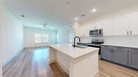 This single-story, 2-bedroom, 3-bathroom home offers a thoughtfully designed layout that balances modern aesthetics with practical living. The open-concept kitchen and living area serves as the heart of the home, featuring light wood-tone flooring, recessed lighting, and a ceiling fan. The kitchen is outfitted with a two-tone cabinet scheme — crisp white upper cabinets paired with slate-gray lower cabinets — complemented by white quartz countertops and a full suite of stainless steel appliances, including a range, microwave, and refrigerator. A central island with an undermount sink adds both prep space and visual appeal. The living area flows seamlessly from the kitchen, benefiting from multiple windows that invite natural light. The bedrooms are carpeted for comfort; the primary bedroom includes a dedicated closet, while the second bedroom features dual windows with outdoor views. The bathrooms are finished with gray shaker-style vanities, white countertops, and wood-look flooring, with the primary bathroom offering a walk-in shower with black-framed glass doors and direct access to a walk-in closet. Two closets throughout the home provide ample storage. A consistent palette of whites, grays, and warm wood tones creates a clean, contemporary ambiance throughout.