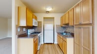 This single-floor residence offers a well-organized and functional layout. The galley-style kitchen is efficiently designed with warm honey-toned wood cabinetry lining both sides, dark granite-style countertops, and a decorative tile backsplash. It is equipped with white appliances including a gas range, over-the-range microwave, refrigerator, and a stainless steel sink. Light hardwood-style flooring runs throughout the kitchen, contributing to a clean and practical workspace.

The living area is generously proportioned, featuring neutral carpet flooring and cream-toned walls that create a bright, open atmosphere. Multiple windows allow natural light to fill the space, and a window air conditioning unit provides climate control. The living area connects seamlessly to the kitchen, offering an open and accessible flow between spaces.

The bedrooms are carpeted and well-sized, with one featuring dual closets for ample storage. Each bedroom includes windows fitted with blinds for privacy and natural light, as well as baseboard heating along the perimeter walls.

The bathroom is finished with light ceramic tile flooring, a vanity with cabinetry, and a tiled shower enclosure. A grab bar is installed near the shower, adding a practical safety feature. The overall space presents a clean, straightforward design with functional finishes throughout.