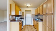 This single-floor residence offers a well-organized and functional layout. The galley-style kitchen is efficiently designed with warm honey-toned wood cabinetry lining both sides, dark granite-style countertops, and a decorative tile backsplash. It is equipped with white appliances including a gas range, over-the-range microwave, refrigerator, and a stainless steel sink. Light hardwood-style flooring runs throughout the kitchen, contributing to a clean and practical workspace.

The living area is generously proportioned, featuring neutral carpet flooring and cream-toned walls that create a bright, open atmosphere. Multiple windows allow natural light to fill the space, and a window air conditioning unit provides climate control. The living area connects seamlessly to the kitchen, offering an open and accessible flow between spaces.

The bedrooms are carpeted and well-sized, with one featuring dual closets for ample storage. Each bedroom includes windows fitted with blinds for privacy and natural light, as well as baseboard heating along the perimeter walls.

The bathroom is finished with light ceramic tile flooring, a vanity with cabinetry, and a tiled shower enclosure. A grab bar is installed near the shower, adding a practical safety feature. The overall space presents a clean, straightforward design with functional finishes throughout.