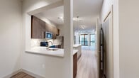 This well-appointed two-bedroom, three-bathroom unit in Houston, TX offers a thoughtfully designed single-level floor plan that maximizes functionality and flow. Light wood-style flooring extends throughout the space, complementing the neutral color palette of white walls and modern finishes.

The kitchen is a standout feature, showcasing dark wood cabinetry with sleek hardware, white quartz countertops, a mosaic tile backsplash, and stainless steel appliances including a refrigerator, microwave, and dishwasher. A peninsula provides additional counter space and opens directly to the living area, which features floor-to-ceiling windows and sliding glass doors leading to a private balcony with outdoor views.

A wide hallway connects the common areas to the private quarters. Both bedrooms feature wood-style flooring and large windows fitted with vertical blinds, allowing ample natural light. The primary bedroom includes direct access to one of the three bathrooms, which features white subway tile surrounding a soaking tub with brushed nickel fixtures. Two dedicated closets provide generous storage. A full-size in-unit washer and dryer are included, adding everyday convenience.