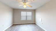 This single-floor residence presents a practical and well-organized layout designed for comfortable everyday living. The kitchen serves as a functional hub, featuring warm wood-toned cabinetry, light countertops, white appliances including a range, microwave, refrigerator, and dishwasher, all set atop durable wood-look flooring. A peninsula counter separates the kitchen from the adjacent living area, creating an open, connected feel with pendant and flush-mount lighting overhead. The living and main areas continue the wood-look flooring, lending a cohesive and easy-to-maintain aesthetic throughout the common spaces. The bedrooms offer a contrasting comfort with plush carpeting underfoot, neutral-toned walls, and ceiling fans with integrated lighting to promote airflow and comfort. Each bedroom benefits from natural light through blinded windows. The bathroom is neatly outfitted with a wood-toned vanity, a large mirror with bar lighting, overhead cabinetry for added storage, and wood-look tile flooring. Throughout the space, clean white trim, neutral wall tones, and consistent finishes create a bright, cohesive atmosphere that is both welcoming and easy to personalize.