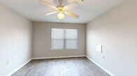 This single-floor residence presents a practical and well-organized layout designed for comfortable everyday living. The kitchen serves as a functional hub, featuring warm wood-toned cabinetry, light countertops, white appliances including a range, microwave, refrigerator, and dishwasher, all set atop durable wood-look flooring. A peninsula counter separates the kitchen from the adjacent living area, creating an open, connected feel with pendant and flush-mount lighting overhead. The living and main areas continue the wood-look flooring, lending a cohesive and easy-to-maintain aesthetic throughout the common spaces. The bedrooms offer a contrasting comfort with plush carpeting underfoot, neutral-toned walls, and ceiling fans with integrated lighting to promote airflow and comfort. Each bedroom benefits from natural light through blinded windows. The bathroom is neatly outfitted with a wood-toned vanity, a large mirror with bar lighting, overhead cabinetry for added storage, and wood-look tile flooring. Throughout the space, clean white trim, neutral wall tones, and consistent finishes create a bright, cohesive atmosphere that is both welcoming and easy to personalize.