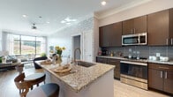 This thoughtfully designed single-floor residence showcases a seamless blend of modern aesthetics and functional living. The open-concept kitchen is a standout, featuring granite countertops, a large center island with an undermount sink, rich dark-toned cabinetry, a decorative tile backsplash, and a full suite of stainless steel appliances. Light wood-style flooring carries throughout the main living areas, complementing the crown molding and neutral color palette.

The living room is anchored by a striking textured accent wall that adds visual depth and dimension. Large floor-to-ceiling windows flood the space with natural light and offer pleasant outdoor views, while a ceiling fan adds comfort. The layout flows naturally between the kitchen and living areas, making it ideal for entertaining.

The bedrooms are generously sized, each featuring plush carpeting, large windows with sheer curtains, and serene, light-filled atmospheres. The primary suite includes access to a well-proportioned walk-in closet with built-in shelving. The en-suite bathroom is elegantly appointed with a double granite vanity, dark cabinetry, decorative wallpaper, and tile flooring. An in-unit laundry area adds everyday convenience. Throughout, crown molding and refined finishes contribute to a cohesive, upscale character.