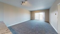 This single-floor residential unit offers a thoughtfully designed layout that balances comfort and functionality. The open-concept living area is generously sized, featuring plush wall-to-wall carpeting and warm neutral-toned walls that create a welcoming atmosphere. Track lighting overhead adds a modern touch, while a sliding glass door leads to a private balcony, offering views of the surrounding urban landscape and filling the space with natural light.

The kitchen is positioned adjacent to the living area and is defined by a breakfast bar counter that provides both a casual dining space and a natural divider. Warm wood cabinetry, granite-style countertops, stainless steel appliances — including a refrigerator, range, and microwave — and wood-look flooring give the kitchen a practical yet polished character. Recessed lighting ensures the workspace is well-illuminated.

The bedroom is a comfortable, carpeted retreat with a large window overlooking the exterior, bringing in ample daylight and views of the neighboring architecture and greenery. The full bathroom is clean and efficiently laid out, featuring a full-size soaking tub with shower, chrome fixtures, and tile flooring. Throughout the unit, white trim and neutral wall tones provide a cohesive, move-in-ready aesthetic.