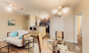 Located at 100 Enterprise Way in Maryville, Tennessee, this single-floor residence offers a well-designed, open-concept layout that seamlessly connects the main living areas. The living room features rich, dark hardwood-style flooring, crown molding, and a ceiling light fixture, creating a comfortable and cohesive atmosphere. Natural light flows in through multiple windows dressed with sheer curtains, lending a bright and airy feel throughout.

The kitchen is a functional centerpiece of the home, equipped with dark espresso cabinetry, black appliances including a refrigerator, electric range, and built-in microwave, as well as a distinctive wine rack cabinet above. A peninsula with bar-height seating provides an ideal casual dining option, while pendant lighting adds a polished touch. The kitchen opens directly to the dining area, which is lit by a chandelier and connects through an arched passage to additional living space.

Both bedrooms are generously sized, each featuring ceiling fans, large windows, and dark hardwood-style flooring. One bedroom includes a private door leading to an outdoor area, while the other offers convenient access to a spacious walk-in closet fitted with wire shelving and hanging rods. An entry area with tall windows invites abundant natural light, completing this well-appointed single-level home.