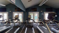 Located at 8301 Paces Oaks Blvd in Charlotte, NC, this single-floor fitness center is a well-equipped facility designed to support a comprehensive workout experience. The space is defined by its bold teal-painted walls, durable tiled flooring, and large wall mirrors that visually expand the room while allowing exercisers to monitor their form.

The cardio zone is generously appointed with multiple treadmills, elliptical machines, and a stationary bike, all positioned to take advantage of natural light streaming in through several large windows and glass French doors. Mounted flat-screen TVs are positioned above the cardio equipment for entertainment during workouts.

The strength training area features a cable cross machine, a dumbbell rack with a variety of free weights, medicine balls, and adjustable workout benches, providing ample options for resistance and functional training. A ceiling fan and overhead lighting ensure the space remains comfortable and well-lit throughout the day.

Natural light plays a significant role in the ambiance of this fitness center, with windows and glass doors offering views of an outdoor patio area with seating. The combination of practical equipment, mirrored walls, and a bright, open layout makes this fitness center a functional and inviting space for residents seeking a convenient on-site workout facility.