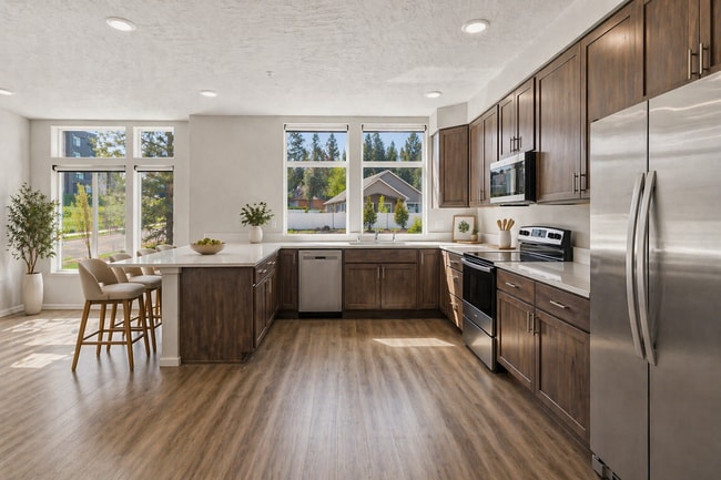 Bright and inviting kitchen with elegant wood cabinetry, sleek stainless steel appliances, and expansive windows offering lush green views. - Lofts at Garden District