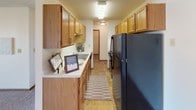 This single-floor unit offers a practical and comfortable layout designed for everyday living. The galley-style kitchen is efficiently arranged with warm wood cabinetry lining both walls, a double-basin sink, light countertops, and tile flooring. Black appliances, including a full-size refrigerator and range, provide functional contrast to the cabinetry. The kitchen opens toward a dining area that transitions seamlessly into the living room, where plush carpeting, a ceiling fan, and a sliding glass door leading to an outdoor patio create a bright and welcoming atmosphere. Baseboard heating is present throughout the unit, ensuring consistent warmth. Two bedrooms, each finished with neutral carpet, textured ceilings, and windows fitted with blinds, offer comfortable private spaces filled with natural light. A full bathroom features a wood vanity with an integrated sink, a large mirror with overhead lighting, tile flooring, and a tub-shower combination. A dedicated utility and storage room with tile flooring and wire shelving provides additional organizational capacity. The unit's neutral color palette and consistent finishes throughout lend it a cohesive, move-in-ready character.